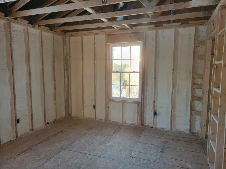 Worker applying spray foam insulation to wall cavity inside a home under construction