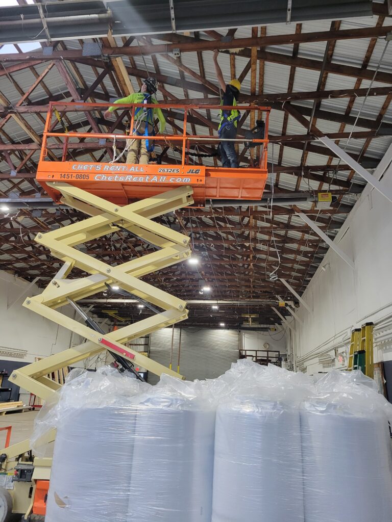 Insulation technicians installing insulation in a commercial building using a scissor lift to improve energy efficiency and building performance