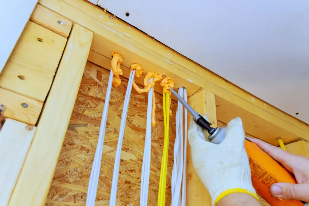 Technician applying spray foam to seal electrical penetrations before adding attic insulation to reduce air leaks and improve energy efficiency.